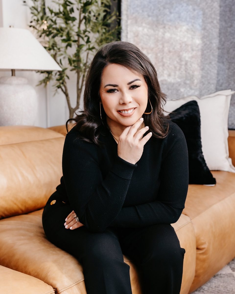 Cherie Garcia seated on a tan leather sofa, smiling, in a black top